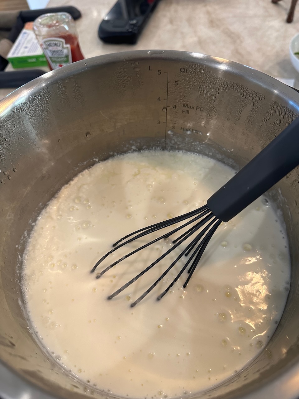 top down view of a stainless steel pot filled with white yogurt, a whisk is partially submerged in it